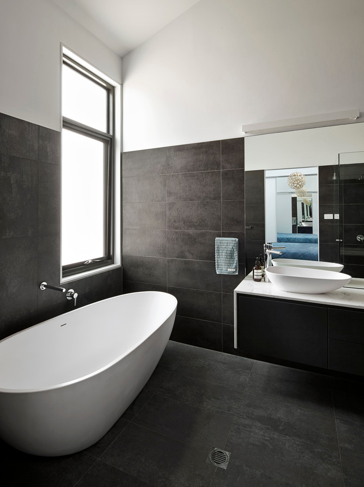 Foto de cuarto de baño principal actual con lavabo sobreencimera, puertas de armario negras, bañera exenta, baldosas y/o azulejos grises, armarios con paneles lisos y paredes blancas