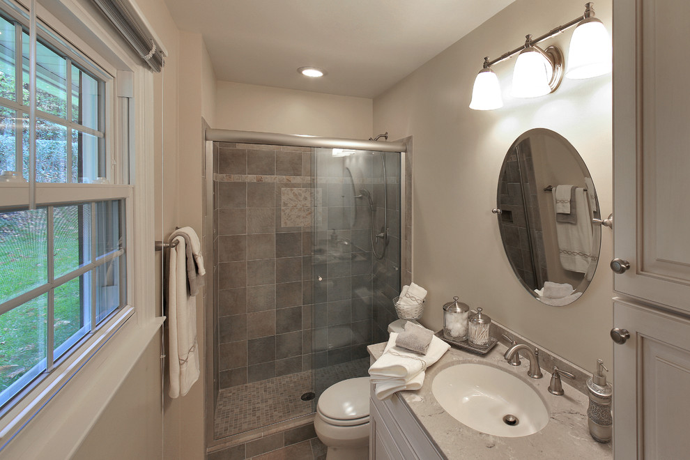 Inspiration for a medium sized traditional shower room bathroom in DC Metro with raised-panel cabinets, white cabinets, a two-piece toilet, brown tiles, porcelain tiles, beige walls, an alcove shower, ceramic flooring, a submerged sink, limestone worktops, brown floors and a sliding door.