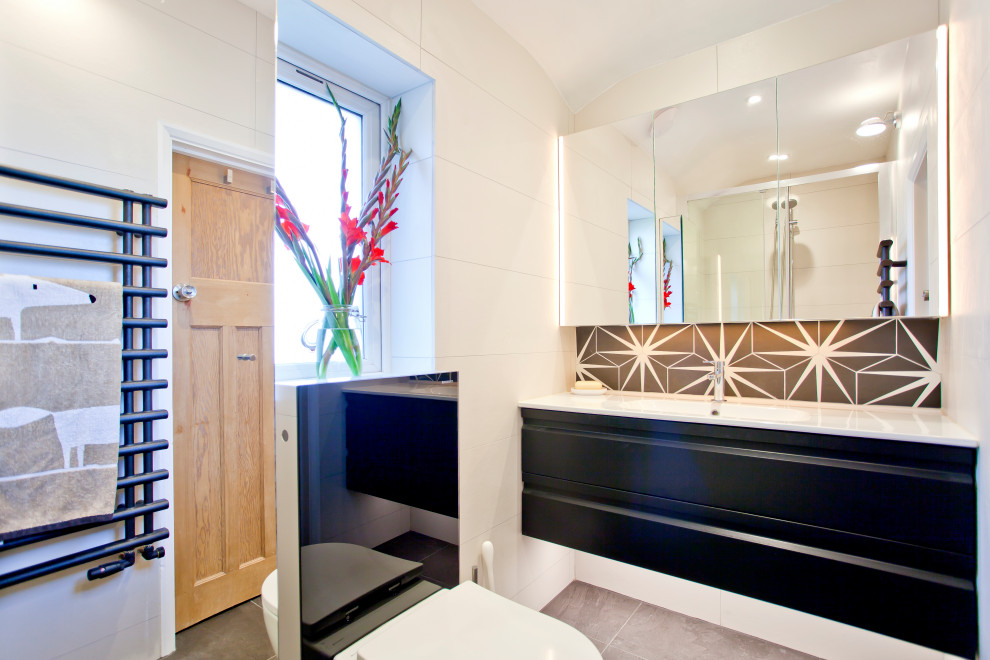 Cette image montre une petite salle de bain minimaliste avec un placard à porte plane, des portes de placard noires, WC suspendus, un carrelage blanc, des carreaux de céramique, un mur blanc, un sol en carrelage de porcelaine, un lavabo suspendu, un sol noir et une cabine de douche à porte coulissante.