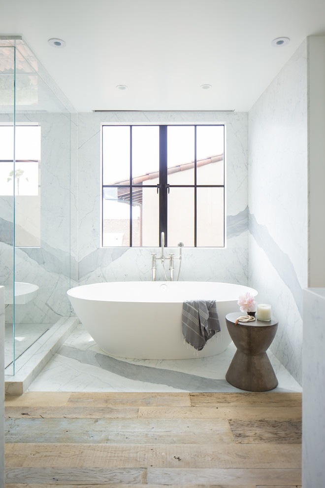 Ejemplo de cuarto de baño actual con bañera exenta, baldosas y/o azulejos blancos, paredes blancas, suelo de madera clara y suelo beige