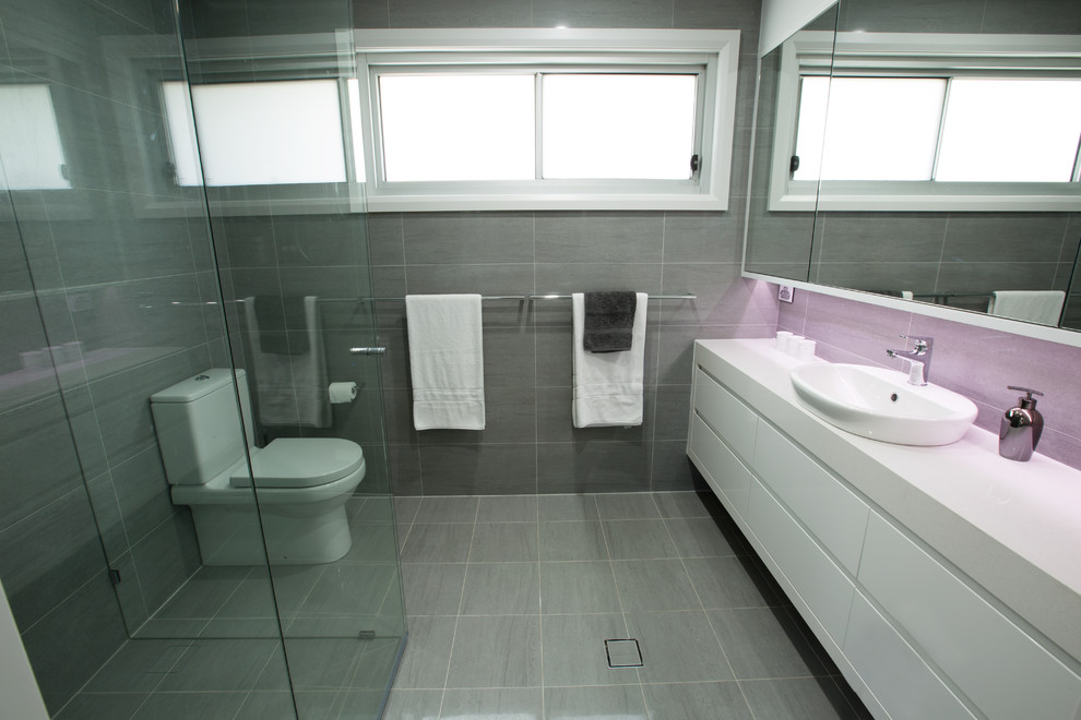 Réalisation d'une salle de bain principale design avec une vasque, un placard à porte plane, des portes de placard blanches, un plan de toilette en quartz modifié, une baignoire indépendante, un carrelage gris, des carreaux de porcelaine, un mur blanc et un sol en carrelage de porcelaine.