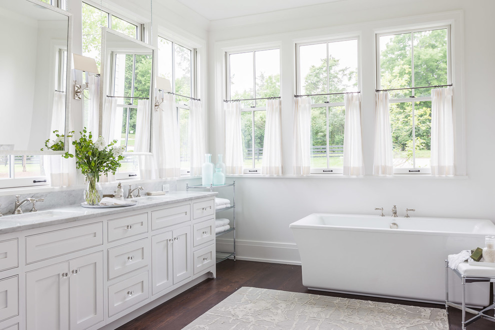 Ispirazione per una stanza da bagno classica con lavabo sottopiano, ante in stile shaker, ante bianche, vasca freestanding, pareti bianche e parquet scuro