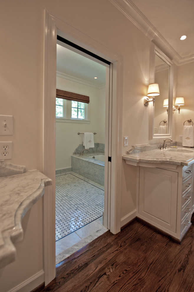 Cette image montre une très grande salle de bain principale traditionnelle avec un lavabo intégré, un placard avec porte à panneau surélevé, des portes de placard blanches, un plan de toilette en marbre, un bain japonais, un mur blanc et un sol en bois brun.