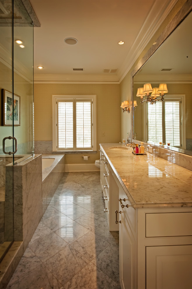 Inredning av ett klassiskt mycket stort en-suite badrum, med ett undermonterad handfat, skåp i shakerstil, vita skåp, marmorbänkskiva, ett platsbyggt badkar, en dusch i en alkov, en toalettstol med hel cisternkåpa, vit kakel, beige väggar och marmorgolv