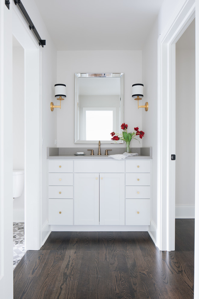Idee per una stanza da bagno tradizionale con ante in stile shaker, ante bianche, pareti bianche, parquet scuro, lavabo sottopiano, pavimento marrone e top grigio