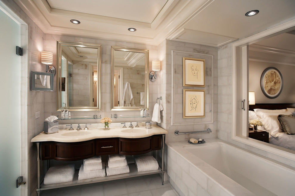 Exemple d'une salle de bain principale chic en bois foncé de taille moyenne avec un placard avec porte à panneau encastré, une baignoire encastrée, du carrelage en marbre, un mur blanc, un sol en marbre, un lavabo encastré, un plan de toilette en marbre et un sol blanc.