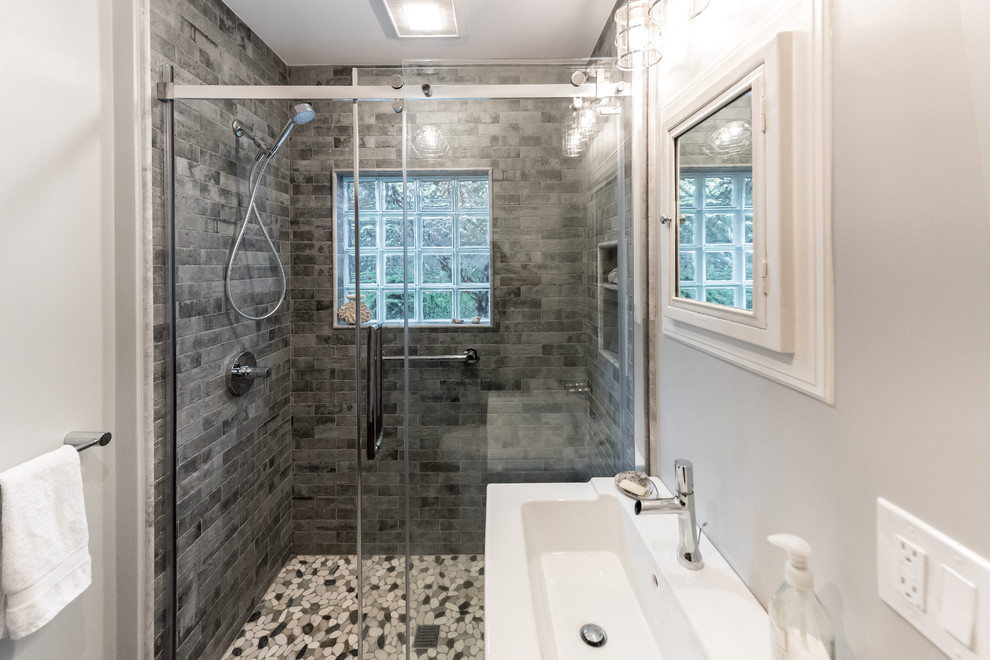 Inspiration for a medium sized contemporary ensuite bathroom in Providence with flat-panel cabinets, dark wood cabinets, a built-in shower, a two-piece toilet, grey tiles, stone tiles, grey walls, pebble tile flooring, a wall-mounted sink, multi-coloured floors, a hinged door and white worktops.