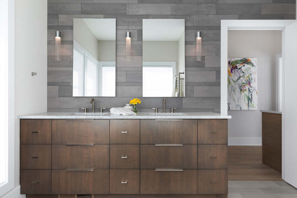 Diseño de cuarto de baño principal y doble contemporáneo con armarios con paneles lisos, puertas de armario de madera en tonos medios, baldosas y/o azulejos grises, paredes grises, suelo gris, encimeras blancas y espejo con luz