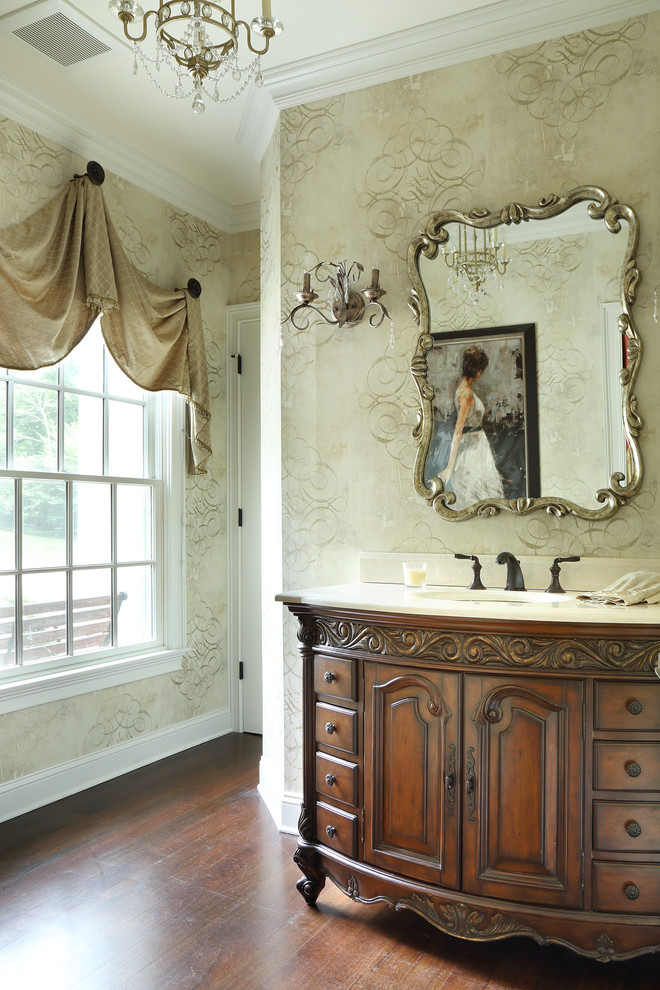 Modelo de cuarto de baño tradicional con lavabo bajoencimera, puertas de armario de madera en tonos medios, paredes beige, suelo de madera oscura y armarios con paneles con relieve