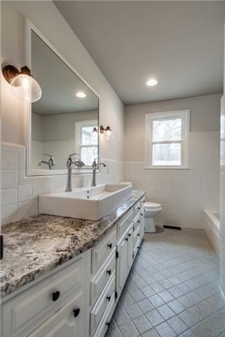 Klassisk inredning av ett mellanstort badrum med dusch, med luckor med upphöjd panel, vita skåp, ett badkar i en alkov, en dusch/badkar-kombination, en toalettstol med hel cisternkåpa, vit kakel, porslinskakel, grå väggar, klinkergolv i porslin, ett avlångt handfat och granitbänkskiva