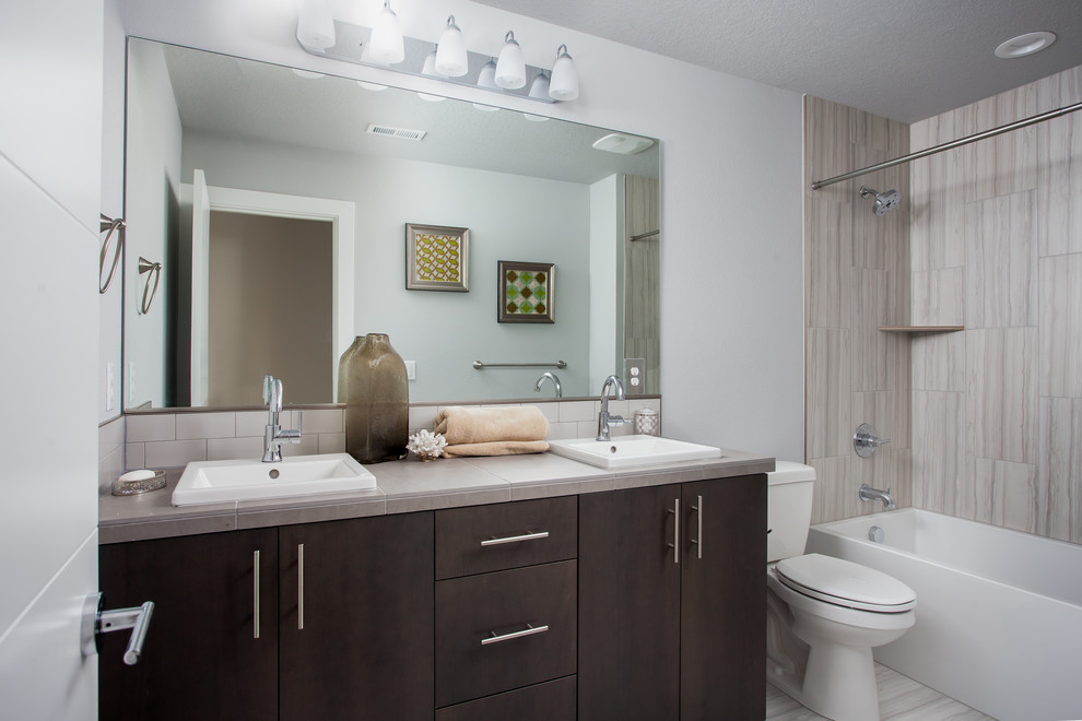 Cette photo montre une salle de bain moderne en bois foncé de taille moyenne avec un placard à porte plane, une baignoire posée, un combiné douche/baignoire, WC séparés, un carrelage beige, un carrelage en pâte de verre, un mur gris, un sol en carrelage de céramique, un lavabo posé, un plan de toilette en carrelage, un sol gris et une cabine de douche avec un rideau.