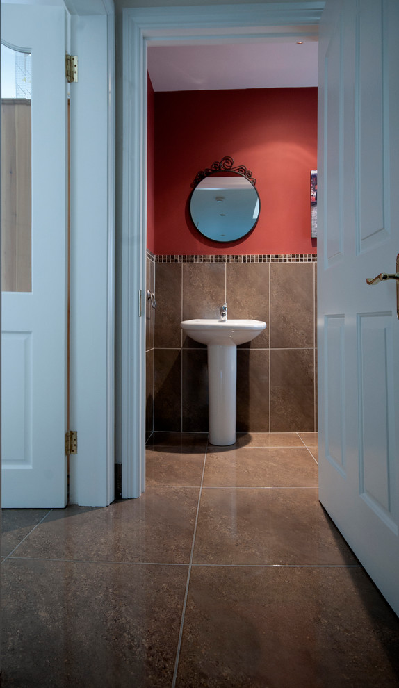 Inredning av ett modernt badrum, med ett piedestal handfat, en toalettstol med hel cisternkåpa, brun kakel, keramikplattor, röda väggar och klinkergolv i keramik