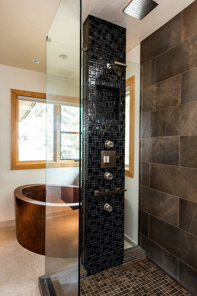 Cette photo montre une salle de bain principale montagne en bois brun de taille moyenne avec un placard à porte plane, une baignoire indépendante, une douche d'angle, un carrelage noir, des carreaux de céramique, un mur beige, un sol en carrelage de porcelaine, un lavabo encastré et un plan de toilette en surface solide.