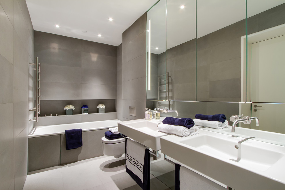 Photo of a contemporary bathroom in London with a wall-mounted sink, a built-in bath, a wall mounted toilet and grey tiles.