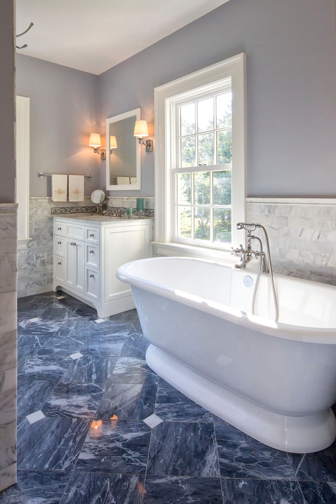 Cette image montre une salle de bain traditionnelle avec une baignoire indépendante, un sol bleu, des portes de placard blanches, un carrelage gris, du carrelage en marbre, un plan de toilette en marbre, un plan de toilette gris, un sol en marbre, un lavabo encastré, un mur bleu et un placard avec porte à panneau encastré.