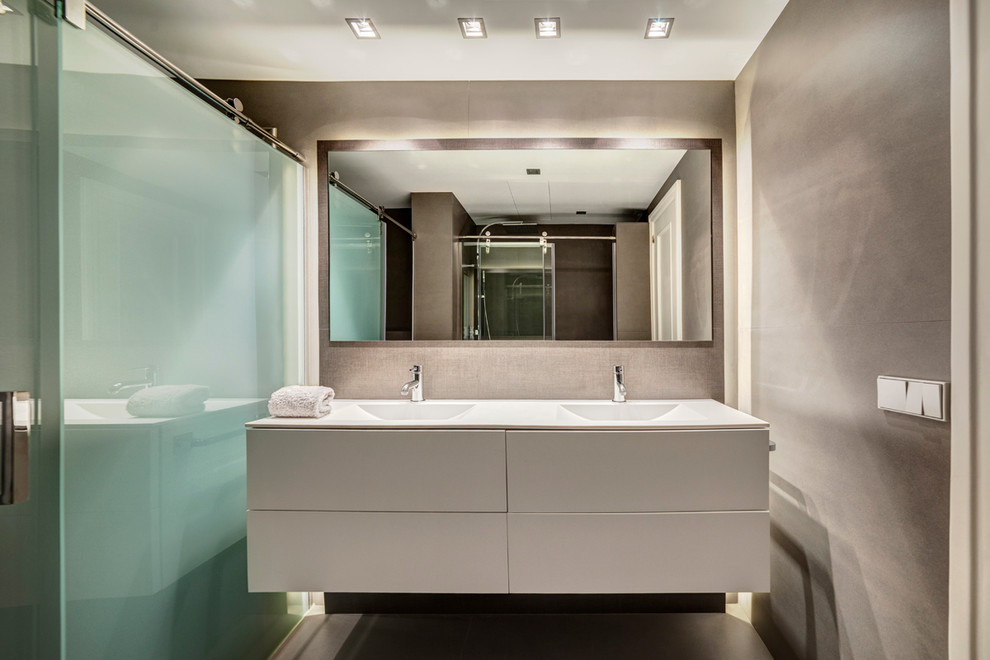 Modelo de cuarto de baño actual de tamaño medio con paredes grises, armarios con paneles lisos, puertas de armario blancas, aseo y ducha, lavabo integrado y encimera de acrílico