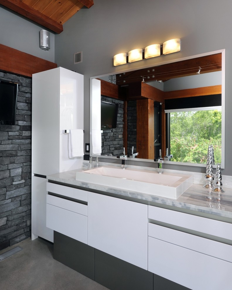 Cette image montre une salle de bain design avec une grande vasque, un placard à porte plane, des portes de placard blanches, un carrelage gris et un carrelage de pierre.