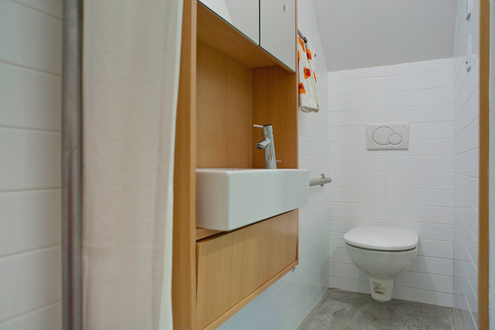 Inspiration pour une salle de bain design en bois brun avec une grande vasque, WC suspendus, un mur blanc, sol en béton ciré, un carrelage blanc et des carreaux de céramique.