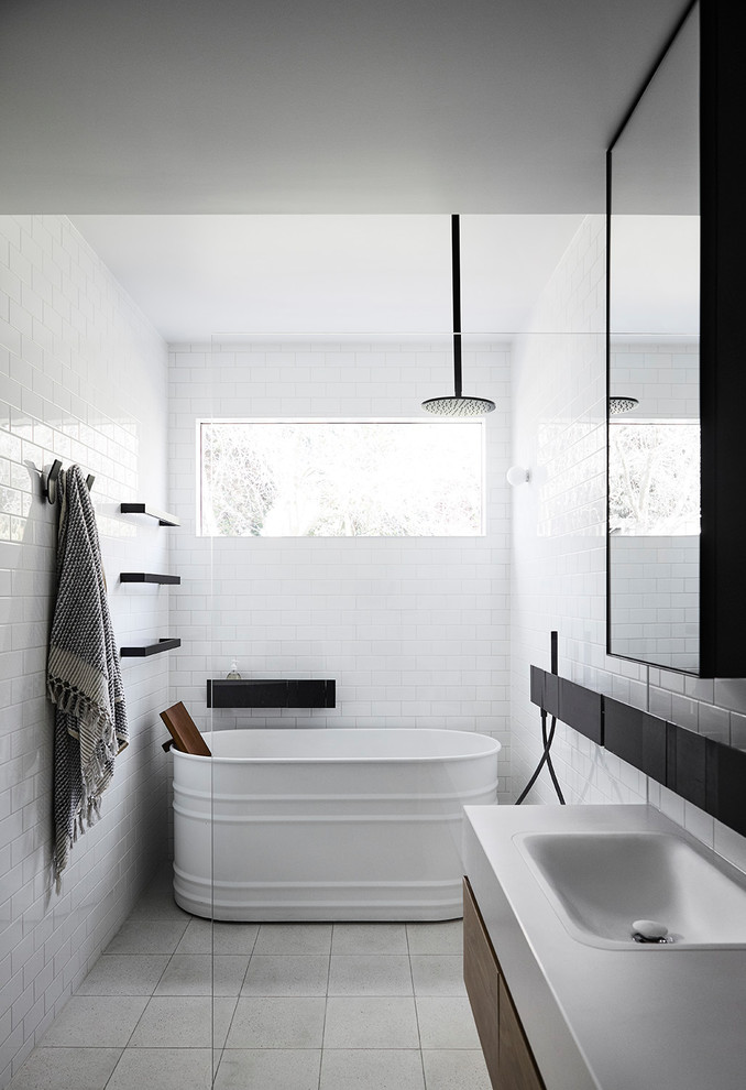 Bild på ett funkis vit vitt badrum, med släta luckor, skåp i mörkt trä, ett fristående badkar, en kantlös dusch, vit kakel, tunnelbanekakel, vita väggar, ett nedsänkt handfat, grått golv och med dusch som är öppen