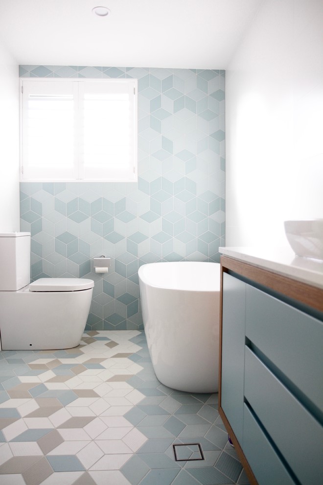 Maritimes Badezimmer mit flächenbündigen Schrankfronten, blauen Schränken, freistehender Badewanne, Toilette mit Aufsatzspülkasten, blauen Fliesen, weißer Wandfarbe, Aufsatzwaschbecken und buntem Boden in Sydney