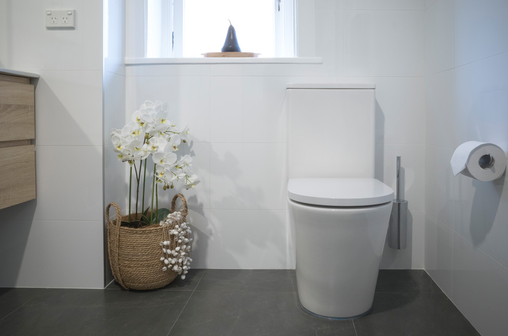 Photo of a medium sized modern ensuite bathroom in Sydney with freestanding cabinets, white tiles, white walls, porcelain flooring, grey floors, an open shower, white worktops, light wood cabinets, a walk-in shower and a two-piece toilet.