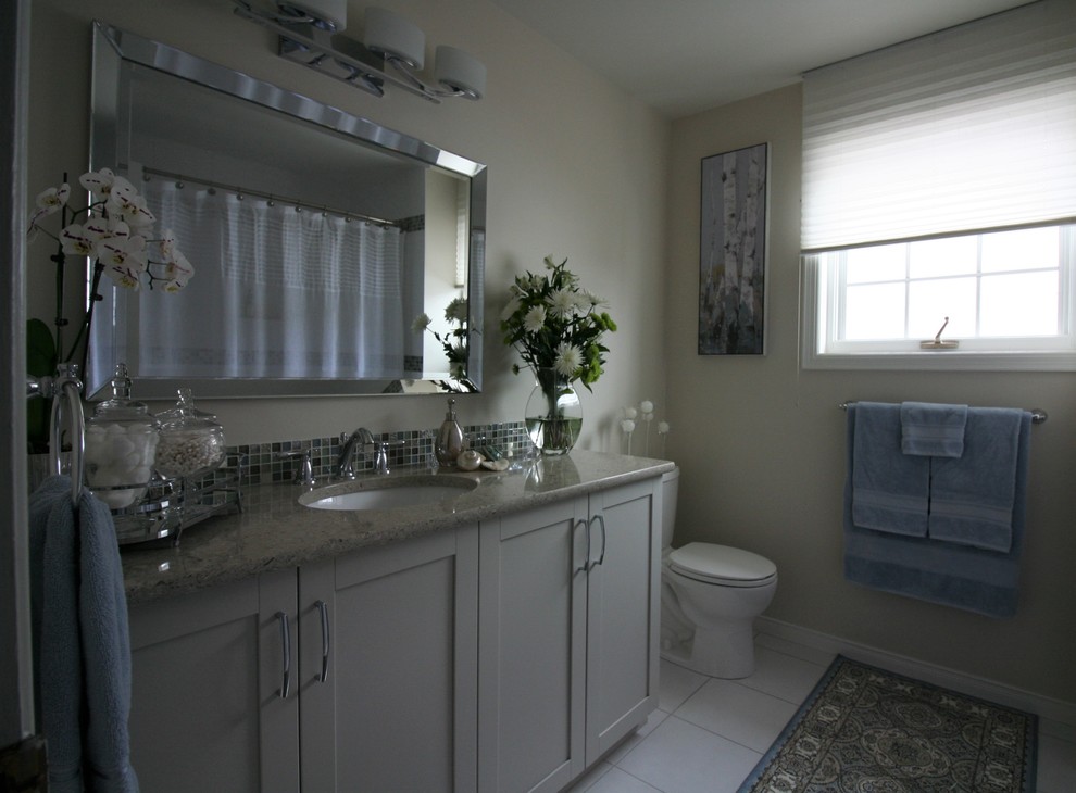 Photo of a medium sized beach style ensuite bathroom in Ottawa with shaker cabinets, beige cabinets, a built-in bath, a two-piece toilet, multi-coloured tiles, glass sheet walls, beige walls, ceramic flooring, a built-in sink, quartz worktops, white floors and beige worktops.