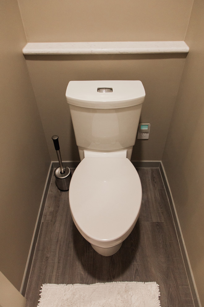 Cette image montre un grand WC et toilettes traditionnel en bois foncé avec un placard à porte plane, WC séparés, un mur beige, sol en stratifié, un lavabo encastré, un plan de toilette en quartz et un sol marron.