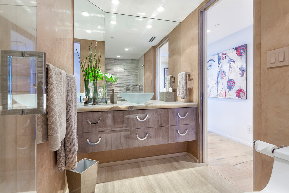 Example of a mid-sized trendy master gray tile and stone tile porcelain tile and beige floor alcove shower design in Miami with flat-panel cabinets, brown cabinets, a one-piece toilet, brown walls, an undermount sink, onyx countertops, a hinged shower door and beige countertops