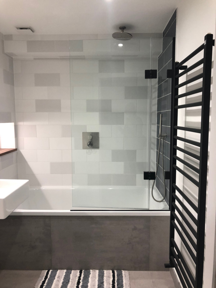 Bild på ett litet nordiskt badrum för barn, med möbel-liknande, vita skåp, ett platsbyggt badkar, en dusch/badkar-kombination, en vägghängd toalettstol, grå kakel, porslinskakel, vita väggar, klinkergolv i porslin, ett väggmonterat handfat och grått golv