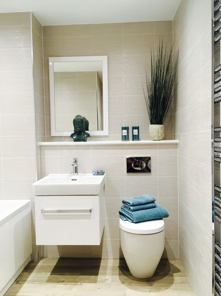 Cette image montre une petite salle de bain design pour enfant avec un placard à porte plane, des portes de placard blanches, une baignoire posée, WC suspendus, un carrelage beige, des carreaux de céramique, un mur beige, un sol en vinyl, un lavabo suspendu et un sol beige.