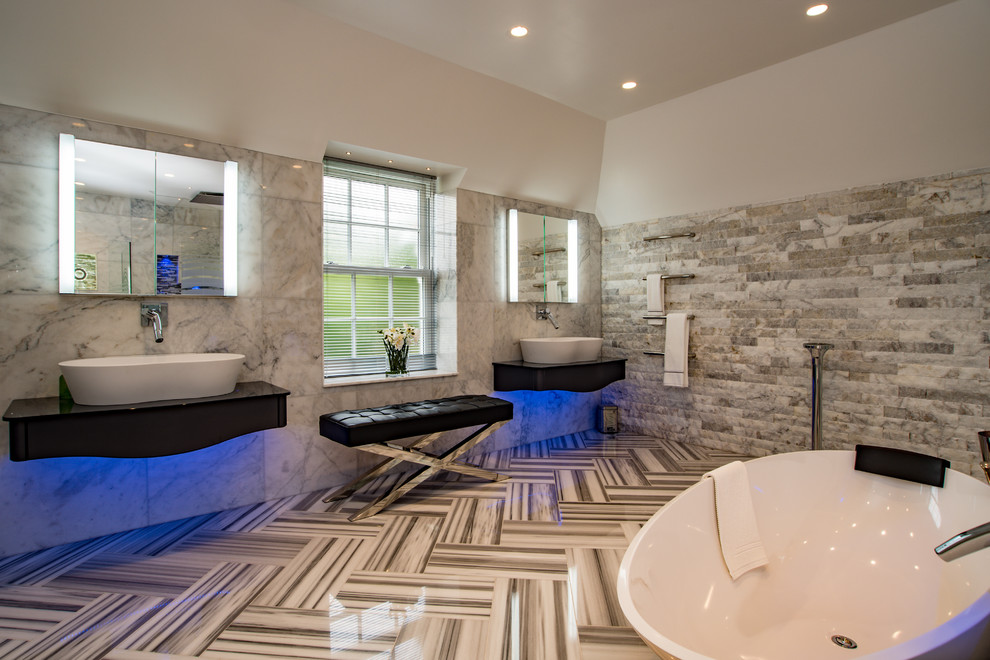 Exemple d'une grande salle de bain principale tendance avec une baignoire indépendante, un carrelage gris, du carrelage en marbre, un mur blanc, un sol en marbre, une vasque, un sol gris et un plan de toilette noir.