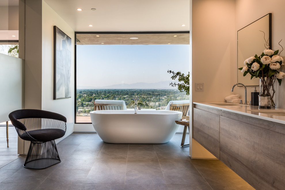 Inspiration for a medium sized contemporary ensuite bathroom in Los Angeles with flat-panel cabinets, light wood cabinets, a freestanding bath, a double shower, a one-piece toilet, brown tiles, stone tiles, white walls, slate flooring, a submerged sink, engineered stone worktops, grey floors, a hinged door and white worktops.
