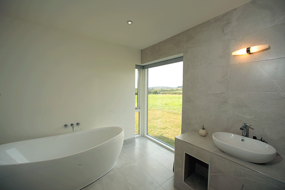 Photo of a medium sized contemporary ensuite bathroom in Cork with a freestanding bath, beige tiles, stone tiles, beige walls, limestone flooring and limestone worktops.