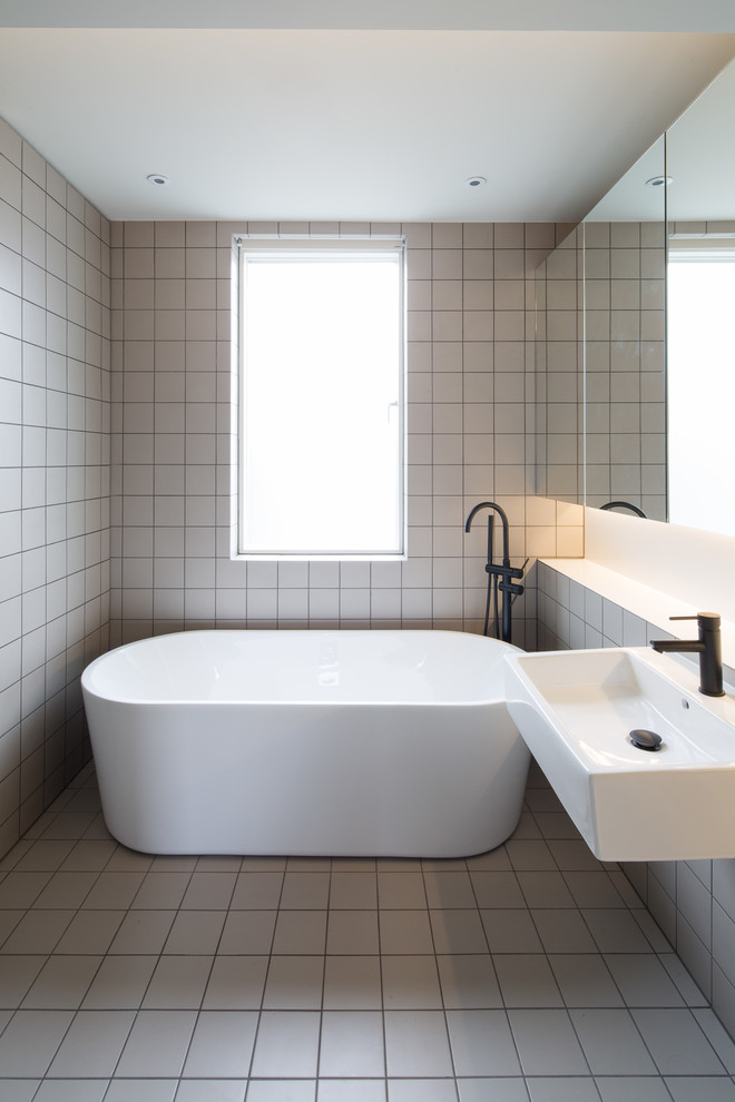 ロンドンにあるコンテンポラリースタイルのおしゃれな浴室 (置き型浴槽、白いタイル、白い壁、壁付け型シンク、白い床) の写真