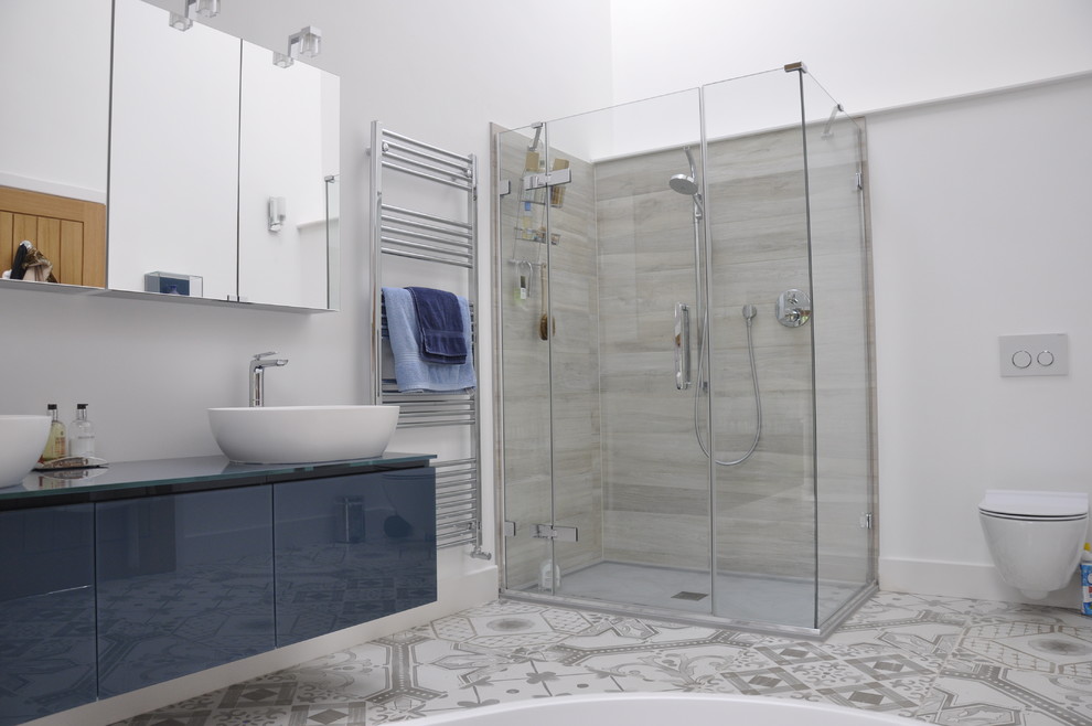 Design ideas for a large contemporary ensuite bathroom in Berkshire with glass-front cabinets, blue cabinets, a freestanding bath, a double shower, a wall mounted toilet, white tiles, porcelain tiles, white walls, ceramic flooring, a vessel sink and glass worktops.