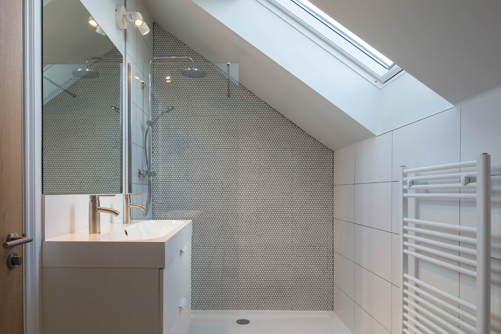 Modern inredning av ett badrum, med släta luckor, beige skåp, en dusch i en alkov, grå kakel, mosaik, vita väggar, ett avlångt handfat och med dusch som är öppen
