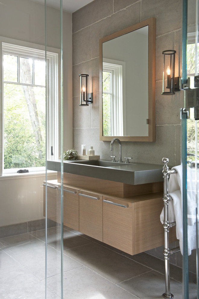Example of a mid-sized transitional master concrete floor freestanding bathtub design in New York with flat-panel cabinets, light wood cabinets, gray walls, an undermount sink and solid surface countertops