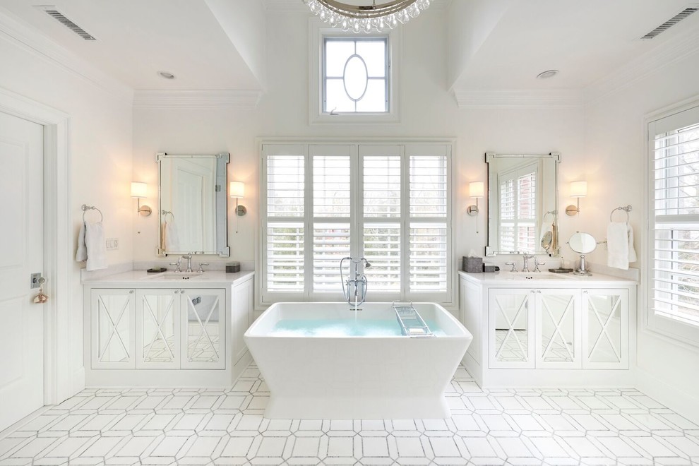 На фото: большая главная ванная комната в классическом стиле с белыми фасадами, отдельно стоящей ванной, врезной раковиной, мраморной столешницей, белыми стенами, разноцветным полом, белой столешницей и зеркалом с подсветкой