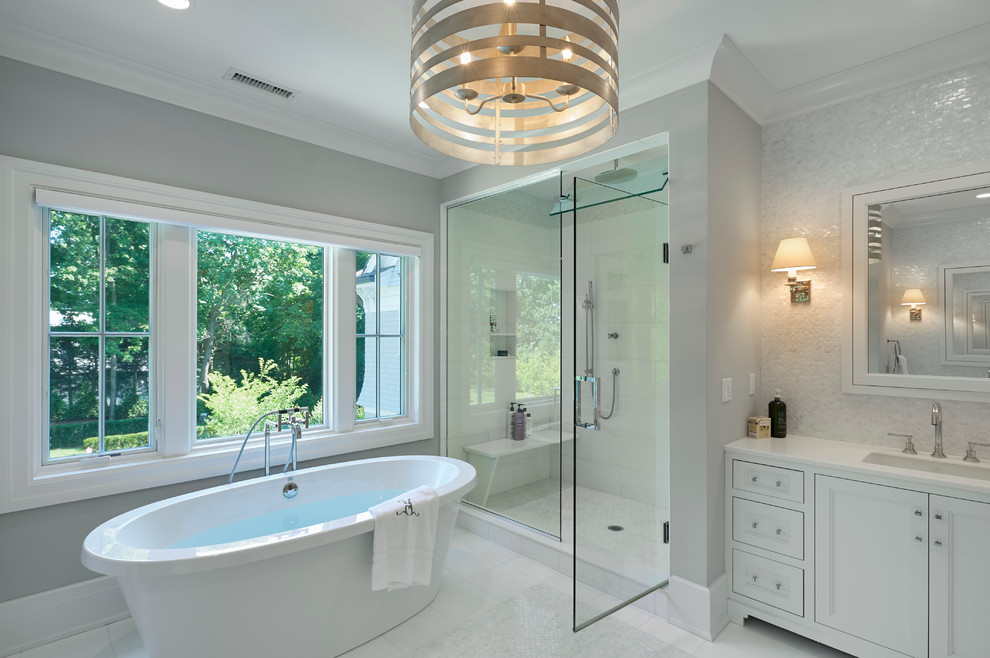 На фото: ванная комната в стиле неоклассика (современная классика) с врезной раковиной, фасадами с утопленной филенкой, белыми фасадами, отдельно стоящей ванной, душем в нише, белой плиткой и серыми стенами с