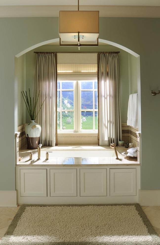 Cette photo montre une salle de bain chic avec des portes de placard blanches, une baignoire encastrée et un carrelage beige.