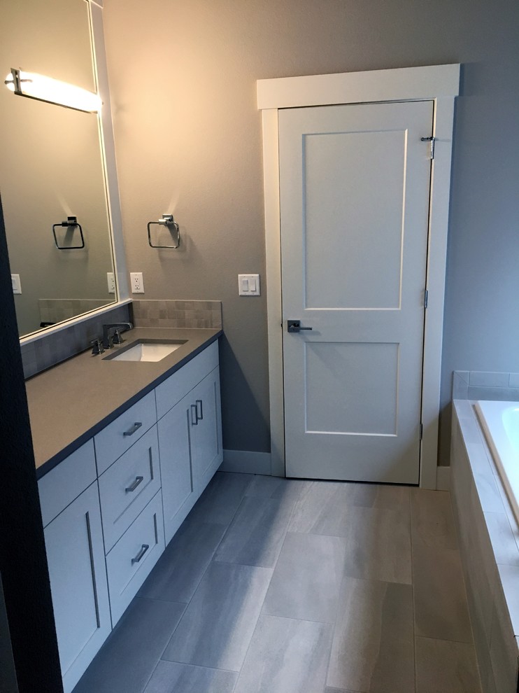 Bild på ett grå grått en-suite badrum, med skåp i shakerstil, vita skåp, ett hörnbadkar, en dusch i en alkov, grå kakel, keramikplattor, grå väggar, klinkergolv i porslin, ett undermonterad handfat, bänkskiva i kvarts och grått golv