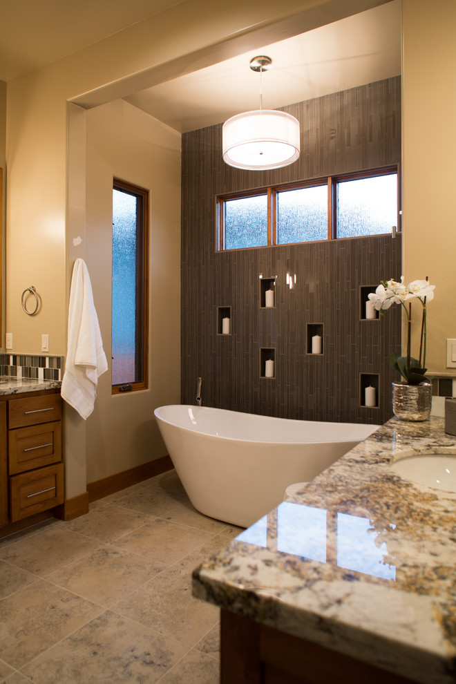 Example of a large trendy master brown tile and matchstick tile porcelain tile and beige floor freestanding bathtub design in Sacramento with shaker cabinets, medium tone wood cabinets, beige walls, an undermount sink, granite countertops and beige countertops