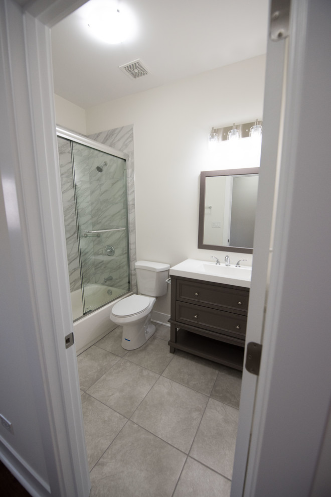 Пример оригинального дизайна: маленькая ванная комната с фасадами в стиле шейкер, коричневыми фасадами, угловым душем, унитазом-моноблоком, бежевой плиткой, мраморной плиткой, белыми стенами, полом из керамической плитки, душевой кабиной, накладной раковиной, серым полом, душем с распашными дверями, зеркалом с подсветкой, тумбой под одну раковину, напольной тумбой и любым потолком для на участке и в саду