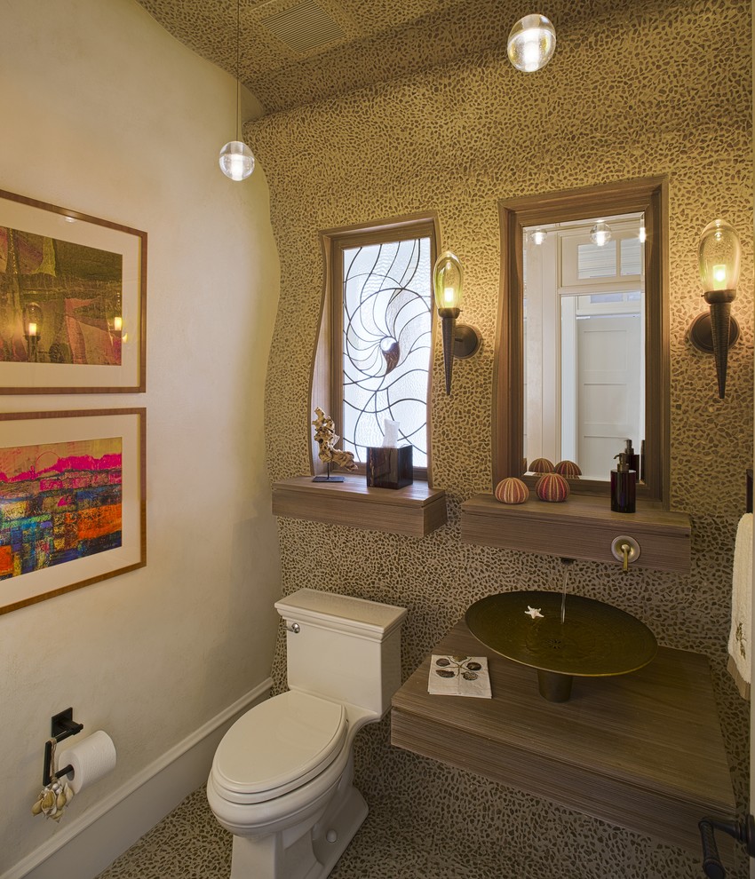 Inredning av ett modernt badrum, med ett fristående handfat, träbänkskiva, kakel i småsten och en toalettstol med hel cisternkåpa