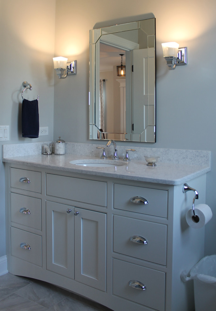 Bild på ett litet amerikanskt badrum, med skåp i shakerstil, vita skåp, ett hörnbadkar, en toalettstol med separat cisternkåpa, grå kakel, porslinskakel, grå väggar, klinkergolv i porslin, ett undermonterad handfat och bänkskiva i kvarts