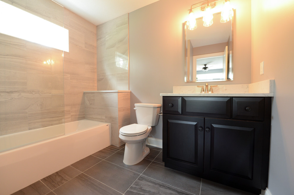 Exempel på ett mellanstort modernt badrum med dusch, med luckor med upphöjd panel, svarta skåp, ett badkar i en alkov, en dusch/badkar-kombination, en toalettstol med separat cisternkåpa, grå väggar, laminatgolv, ett undermonterad handfat, marmorbänkskiva, grått golv och dusch med skjutdörr