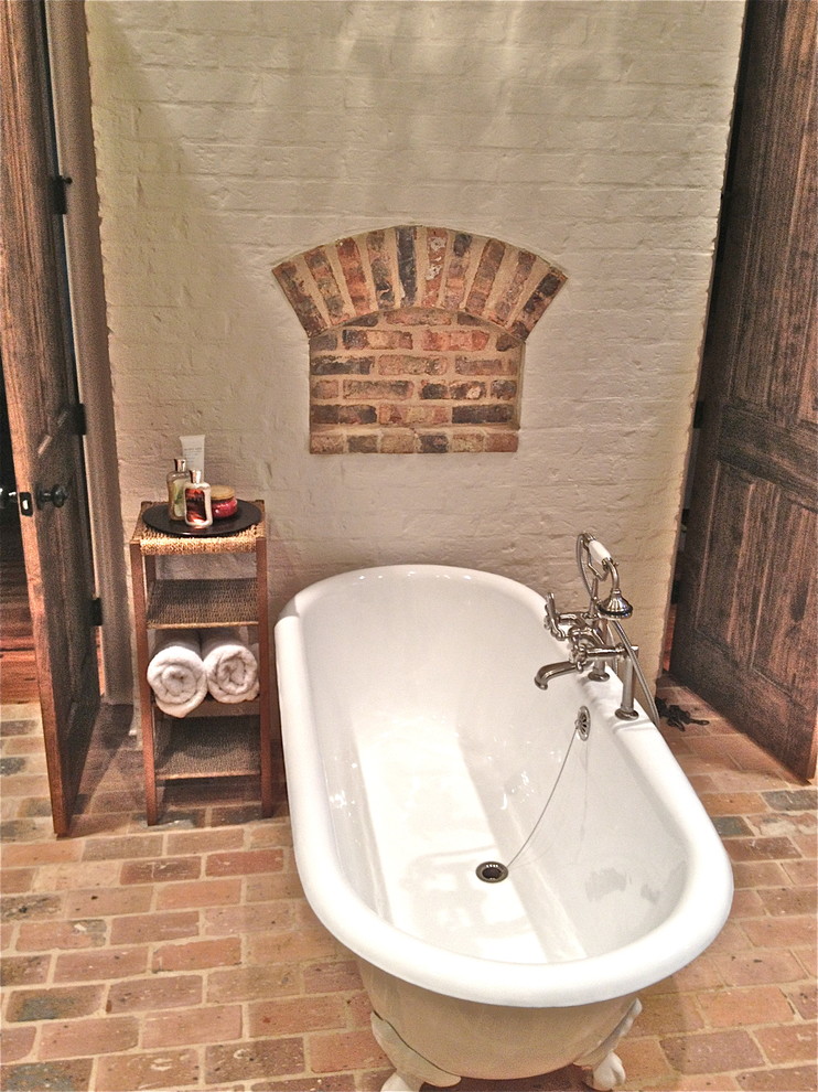 Immagine di una stanza da bagno padronale stile rurale con vasca con piedi a zampa di leone e pavimento in mattoni