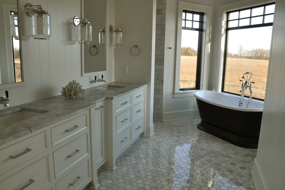 На фото: большая главная ванная комната в стиле неоклассика (современная классика) с белыми фасадами, отдельно стоящей ванной, открытым душем, серой плиткой, каменной плиткой, серыми стенами, полом из керамической плитки, серым полом и открытым душем с