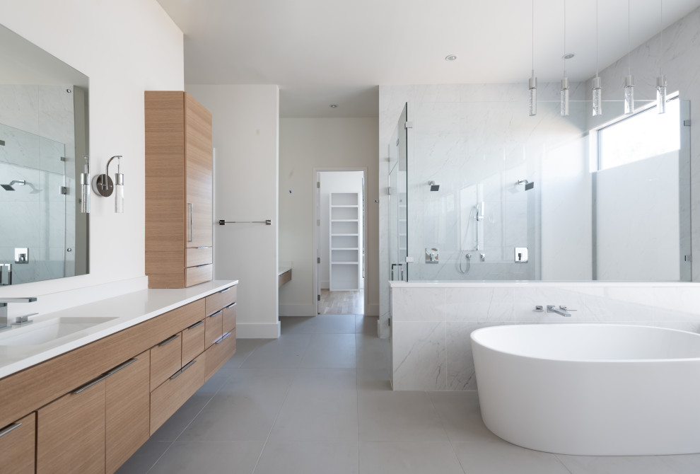 This is an example of a large traditional ensuite bathroom in Dallas with flat-panel cabinets, light wood cabinets, a freestanding bath, a double shower, grey tiles, white walls, porcelain flooring, a submerged sink, grey floors, a hinged door, white worktops, a single sink and a floating vanity unit.