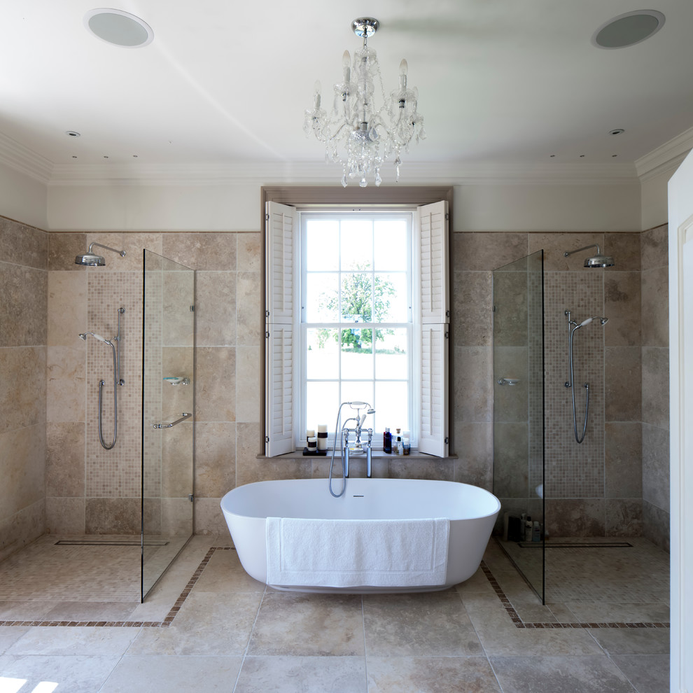 Klassisk inredning av ett badrum, med ett fristående badkar, en dubbeldusch, beige kakel och travertinkakel